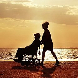 Woman pushing a man in a wheelchair on a beach at sunset