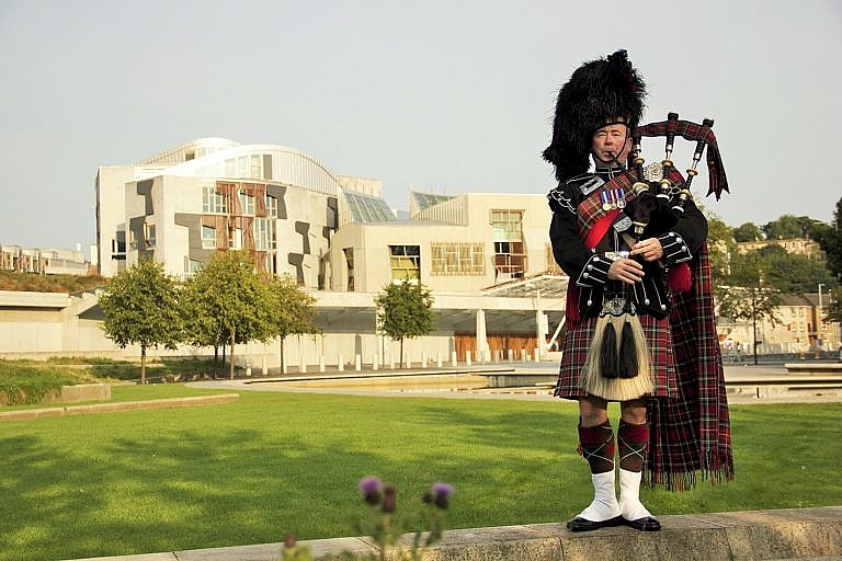 Bagpipe player standing before the Scottish parliament building.
